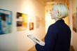 Side view portrait of mature female manager holding clipboard working in art gallery, copy space