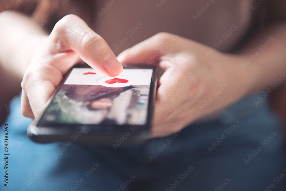Finger of woman pushing heart icon on screen in mobile smartphone application. Online dating app, valentine's day concept. - obrazy, fototapety, plakaty 