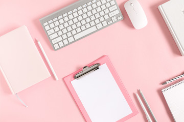 Home office pink table, notepad, clipboard, keyboard, diary, notebook, stationery on pink background. Flat lay, top view, copy space 