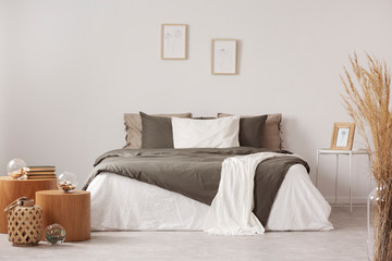 Wooden tables next to brown and white bed in natural bedroom interior with posters. Real photo