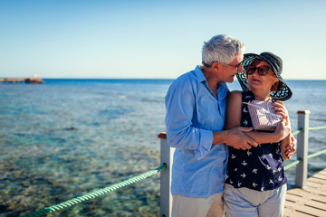 Wall Mural - Senior couple walking on pier by sea presenting gifts for Valentine's day. People enjoying vacation.