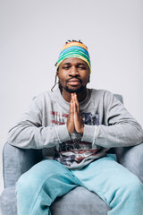 Wall Mural - Portrait of a smiling black young model in a gray sweater and blue pants on a gray background near the chair