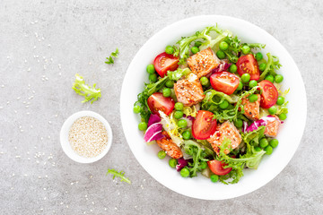 Healthy lunch vegetable salad with baked salmon fish, fresh green peas, lettuce and tomato. Top view