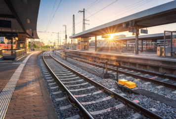 Wall Mural - Railway station at sunset. Industrial landscape with railroad, railway platfform, buildings, blue sky with orange sunlight in the evening. Railway junction in summer in Europe. Transportation