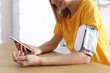 © New Africa - Woman checking blood pressure with modern monitor and smartphone at table indoors, closeup. Cardiology concept