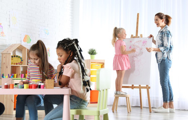 Poster - Female teacher with child near easel at painting lesson indoors