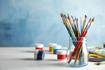 Poster - Glass jar with brushes and paints on table against color background. Space for text