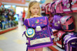 Cute little girl choosing a schoolbag before starting classes. Adorable pupil buying school backpack in a store.
