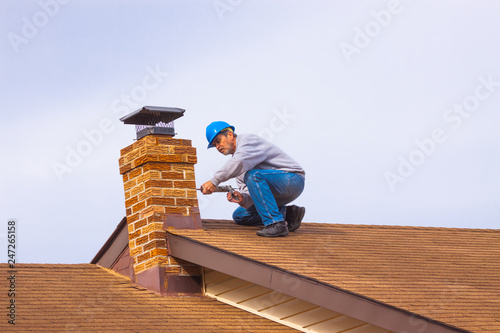 Fotografía Contractor Builder with blue hardhat on the roof caulking chimney