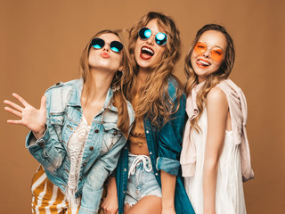 Wall Mural - Three beautiful smiling hipster girls in trendy summer casual clothes and sunglasses. Sexy carefree women posing near golden wall. Positive models going crazy. Showing tongue