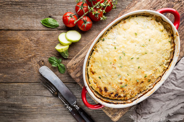 Wall Mural - Casserole with chicken and zucchini on old wooden background, top view