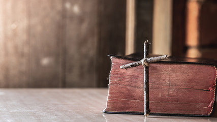 wooden cross with bible on wooden table with window light, christian concept.