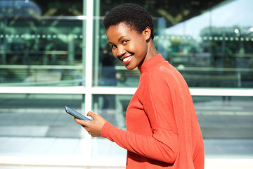 Wall Mural - beautiful young african american woman holding cellphone and smiling