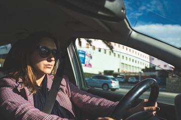 Girl driving her car on sunny day. Woman holding the serious steering wheel inside the vehicle and alternative means transportation of application