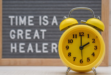 yellow alarm clock on the background of a sign with the inscription time is a great healer