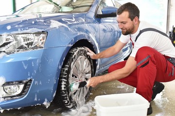 customer service in the car trade: worker cleaning a vehicle // Kundendienst in der Autowerkstatt: fröhlicher Arbeiter renigt ein Fahrzeug und die Felgen