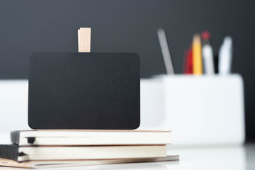 Poster - close up clip blackboard on notebook with blur modern pencil box  on table and dark grey wall in office desk,mock up space for display of design or text.