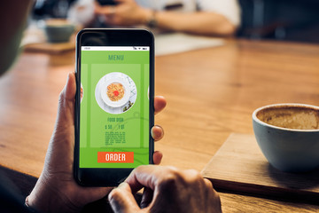 Poster - Close up woman hand holding food online mobile apps with hot coffee cup on table sitting at coffee shop,online order concept.