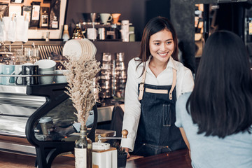Poster - Asian woman barista wear jean apron holding coffee cup served to customer at bar counter with smile emotion,Cafe restaurant service concept,Owner small business concept.