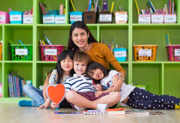 Wall Mural - Asian female teacher teaching hug mixed race group of  kids  in classroom,Kindergarten pre school concept.