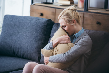 Wall Mural - sad woman sitting on couch, crying and holding pillow at home