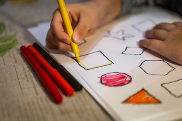 child painting and coloring figures on white sheet at home. 