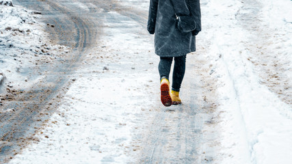 Wall Mural - Winter Walk in Yellow Leather Boots. Back view on the feet of a women walking along the icy snowy pavement. Pair of shoe on icy road in winter. Abstract empty blank winter weather background