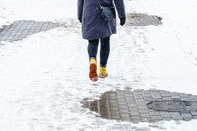 Winter Walk In Yellow Leather Boots. Back View On The Feet Of A Women Walking Along The Icy Snowy Pavement. Pair Of Shoe On Icy Road In Winter. Abstract Empty Blank Winter Weather Background