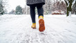 © v_sot - Winter Walk in Yellow Leather Boots. Back view on the feet of a women walking along the icy snowy pavement. Pair of shoe on icy road in winter. Abstract empty blank winter weather background
