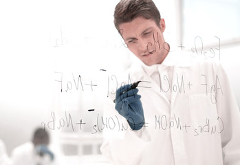 serious scientist writes a formula on a glass Board