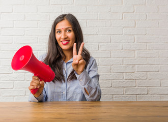 Young indian woman showing number two, symbol of counting, concept of mathematics, confident and cheerful. Holding a megaphone.