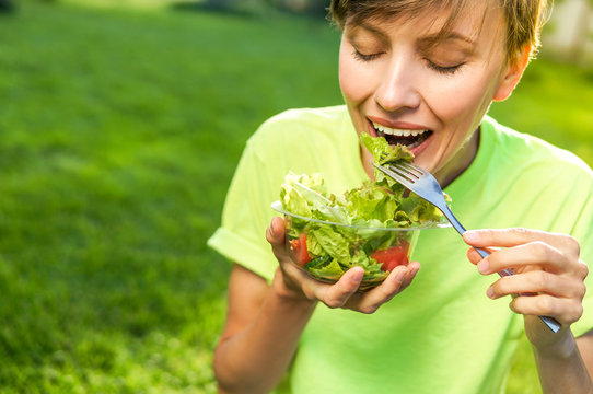 beautiful caucasian woman eating salad over green natural background