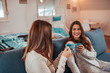 © bnenin - Two female friends or sisters laughing. Casual millennial women drinking tea at home.
