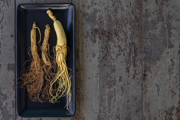 Wall Mural - Fresh and dry ginseng on black plate with copy space on the wood background.