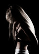 © Алексей Торбеев - Beautiful slim topless blonde girl with hair falling on her face, stands sideways with a her hand covering her big boobs. Black background. Artistic noir silhouette photo