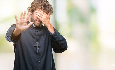 Wall Mural - Handsome hispanic catholic priest man over isolated background covering eyes with hands and doing stop gesture with sad and fear expression. Embarrassed and negative concept.