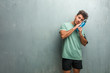 © Asier - Young fitness man against a grunge wall tired and very sleepy, looking comfortable and relaxed, sleep gesture. Holding a blue energy drink.