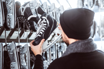 Wall Mural - A young guy wearing warm clothes standing next to a rack and choosing a pair of skates in a skate hire inside.