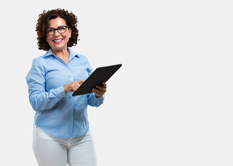 Middle aged woman smiling and confident, holding a tablet, using it to surf the internet and see social networks, communication concept