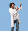© Asier - Handsome african american medical doctor pointing to the side, smiling surprised presenting something, natural and casual