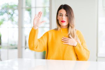 Young beautiful woman wearing winter sweater at home Swearing with hand on chest and open palm, making a loyalty promise oath