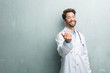 Young friendly doctor man against a grunge wall with a copy space inviting to come, confident and smiling making a gesture with hand, being positive and friendly