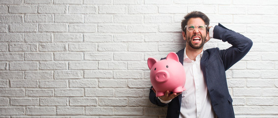 Young business man wearing a suit against a white bricks wall crazy and desperate, screaming out of control, funny lunatic expressing freedom and wild