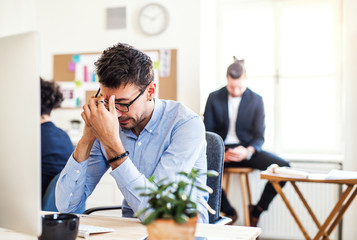 Young frustrated businessman with smartphone working in a modern office.