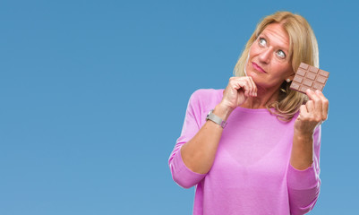 Canvas Print - Middle age blonde woman eating chocolate bar over isolated background serious face thinking about question, very confused idea