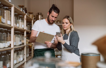 Two shop assistants standing at the counter in zero waste shop, checking stock.