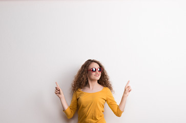 Wall Mural - A young beautiful cheerful woman with red sunglasses in studio. Copy space.