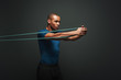 © Friends Stock - Get stronger every day. Sportsman working out with resistance band over dark background