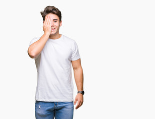 Young handsome man wearing white t-shirt over isolated background covering one eye with hand with confident smile on face and surprise emotion.