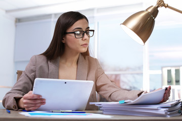 Businesswoman working with tablet and documents at table in office